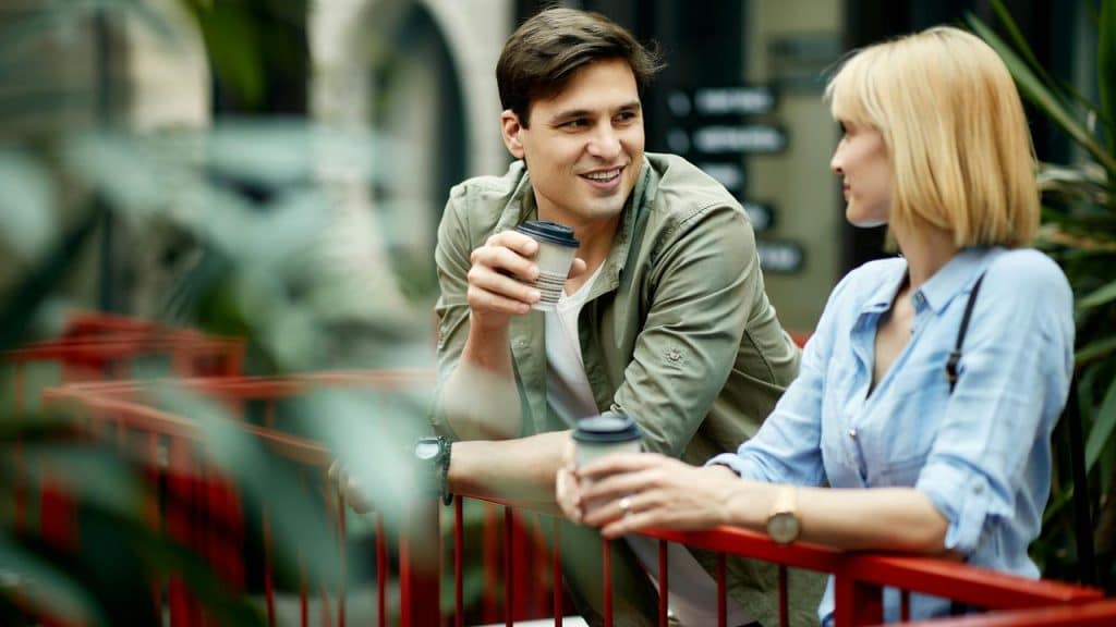 A man and woman chatting while holding coffee cups outdoors.