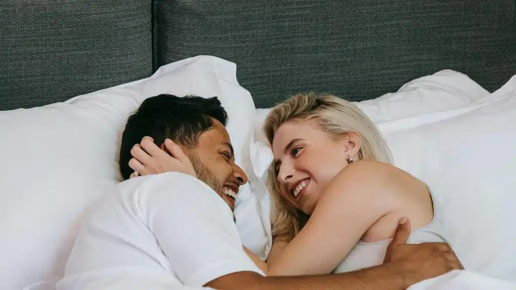 A couple lying in bed smiling at each other.