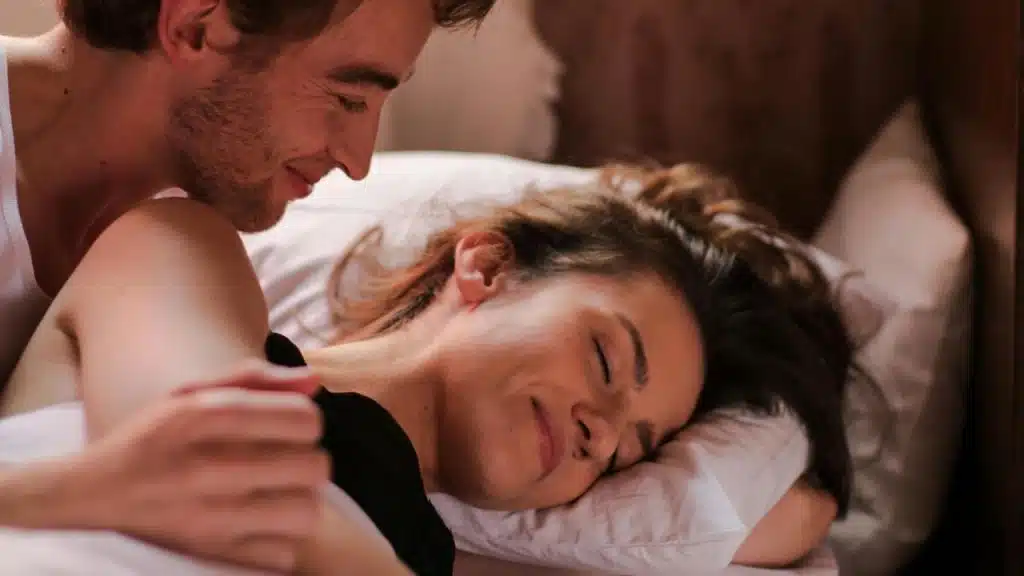 A man gently holding a smiling woman lying in bed.