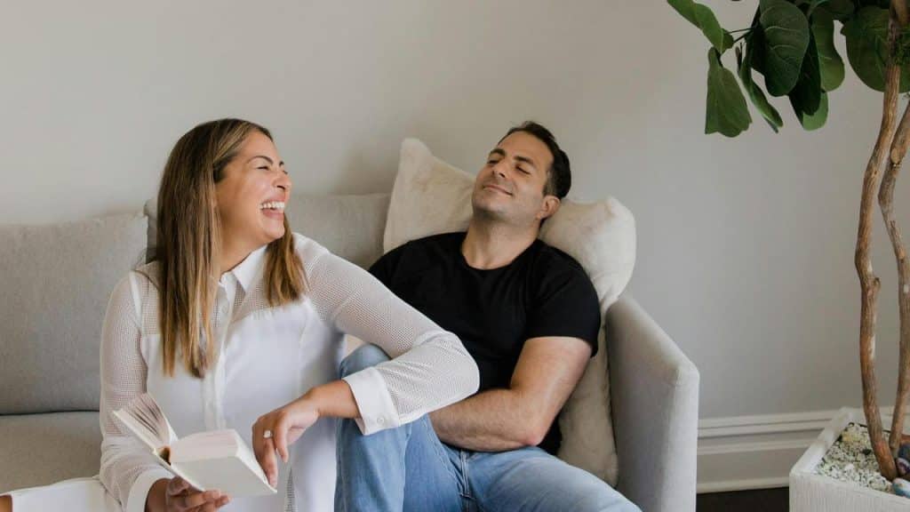 A woman laughing while sitting next to a relaxed man on a couch.