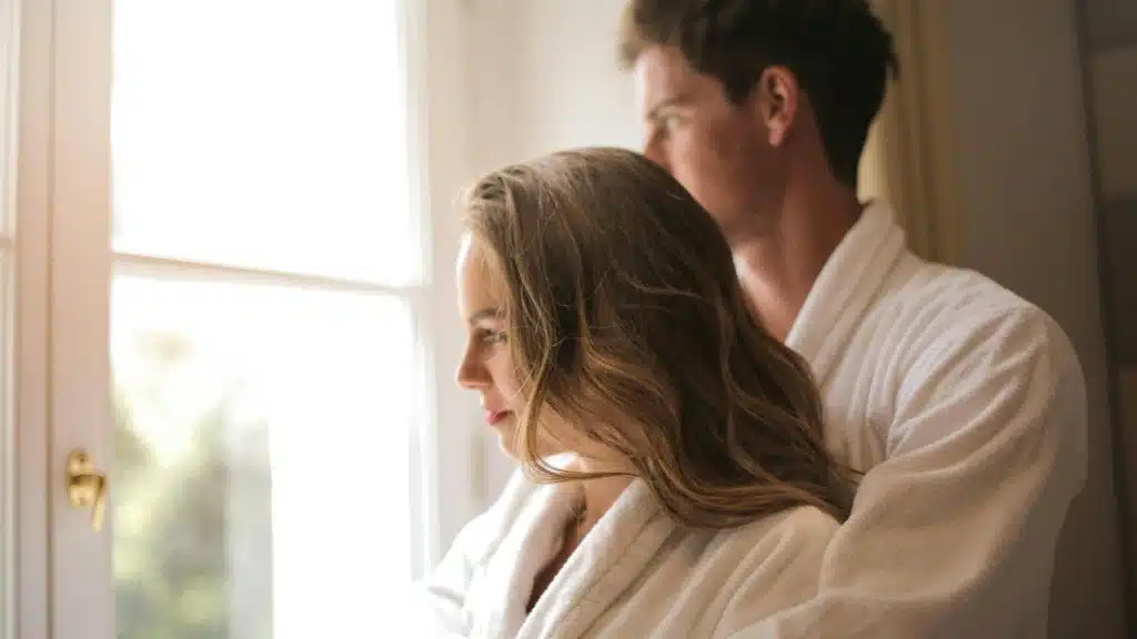A couple in white robes standing by a window looking outside.