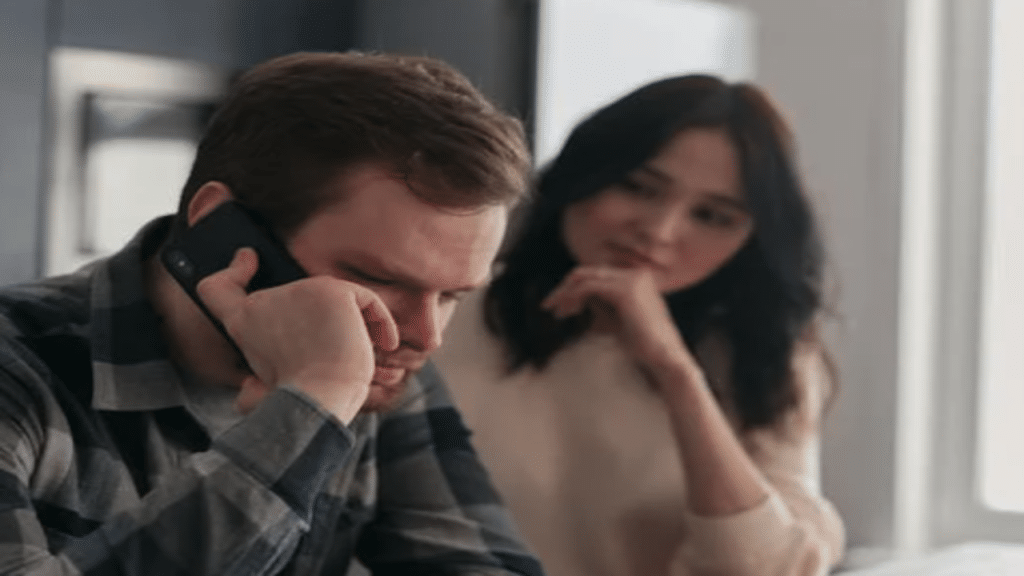 A man on the phone while his wife tries to talk to him