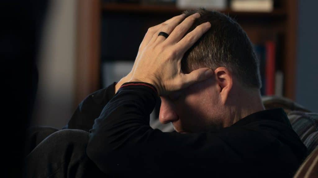 Man seated with his head in his hands, wearing a black shirt and ring.