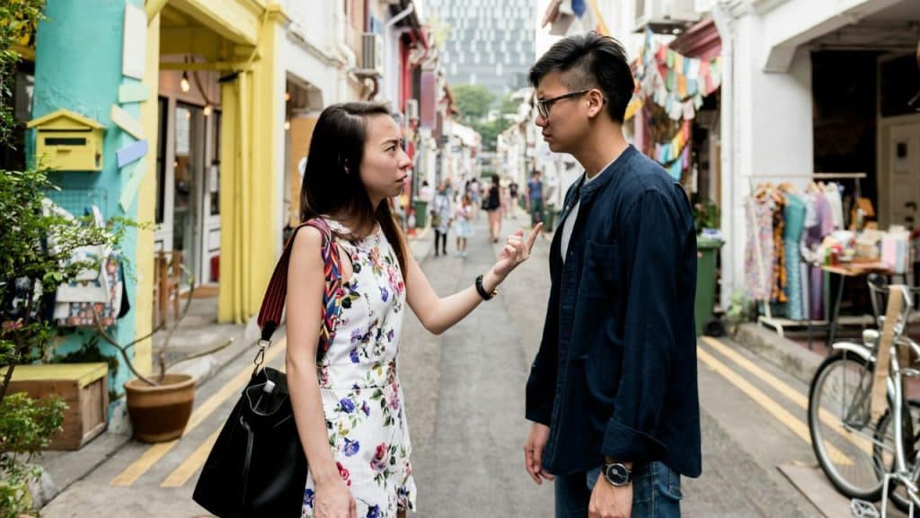 A woman in a floral dress argues with a man on a narrow, colorful street.