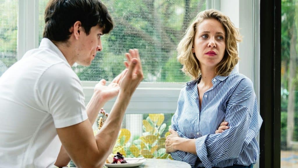 A man gestures while talking to a woman with her arms crossed who looks upset.