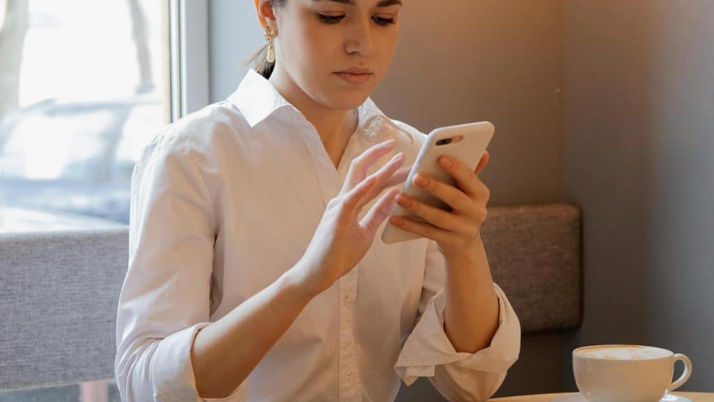 A woman in a white shirt using her phone at a café table.