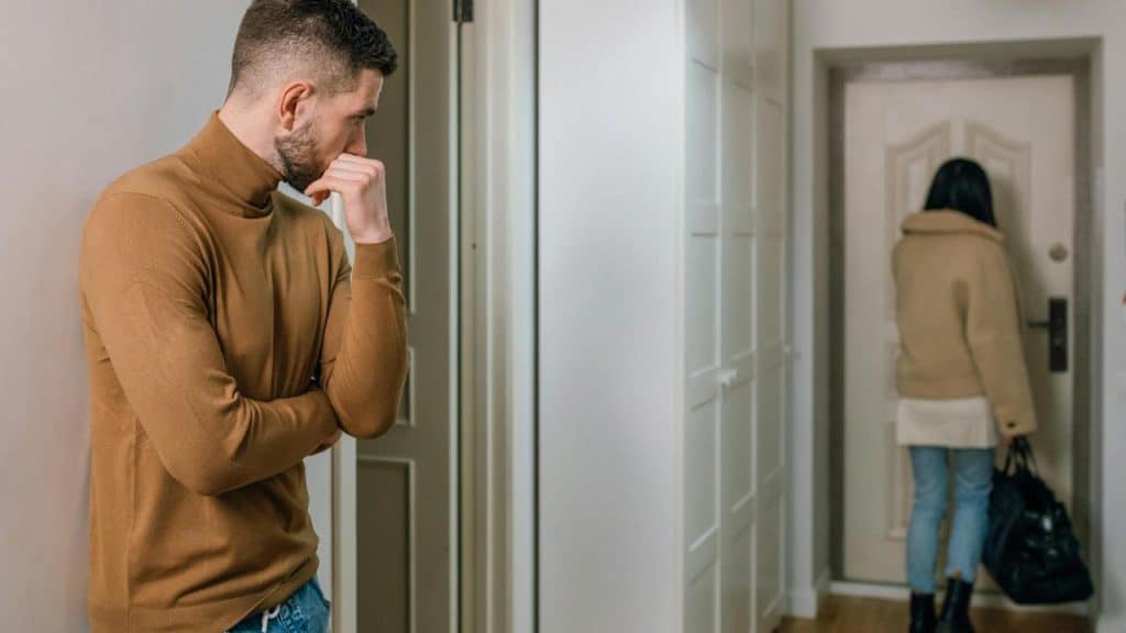 A man standing thoughtfully as a woman walks toward the door.