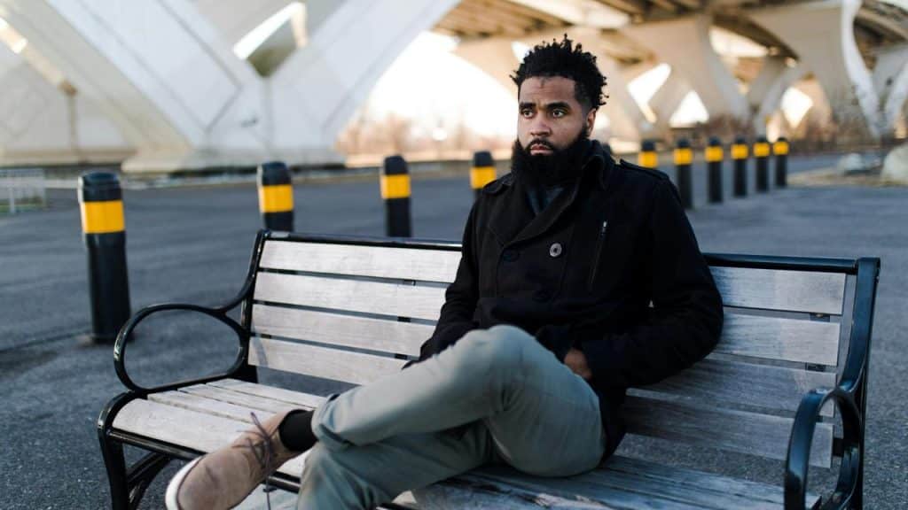 A man sitting on a bench outdoors with his legs crossed.