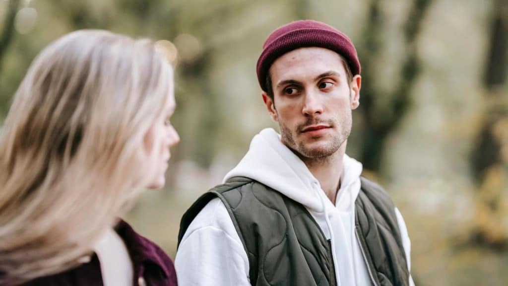 A man in a beanie looking at a woman outdoors.