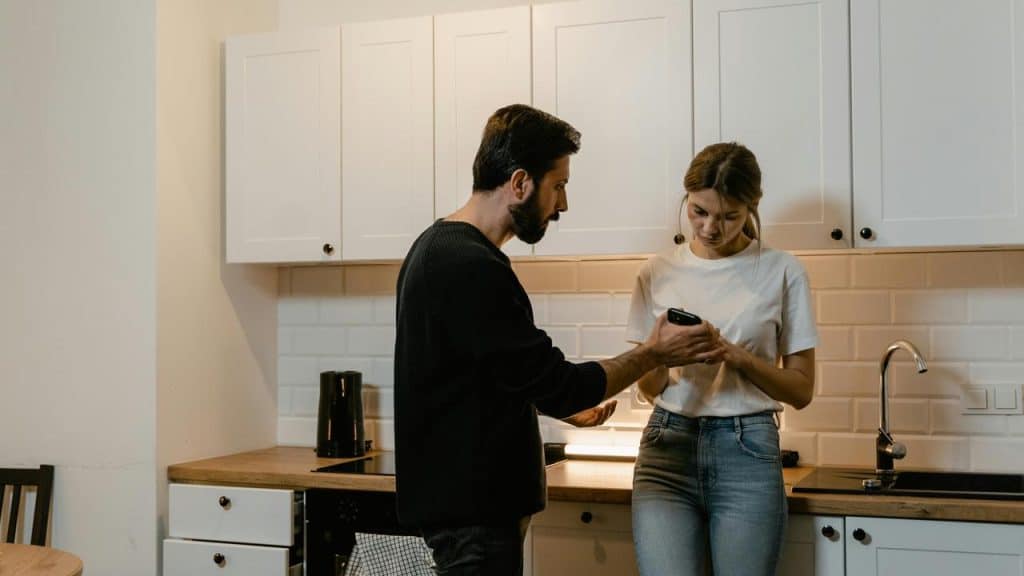 A man showing something on a phone to a woman in a kitchen.