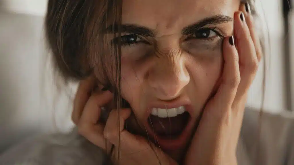 A woman with an angry expression holding her face.