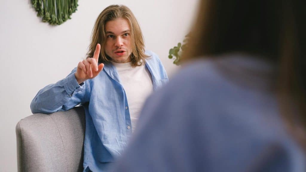 A man sitting and pointing his finger while talking to someone.