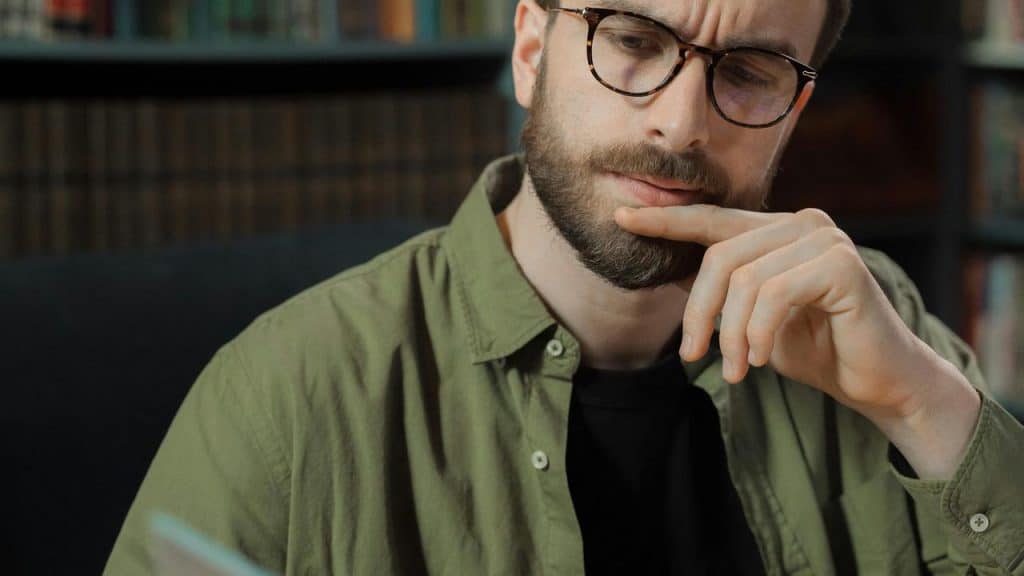 A man wearing glasses looking thoughtful while holding his chin.