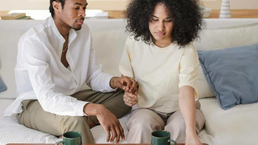 A man holding a woman’s hand while she reaches for her phone at a table.