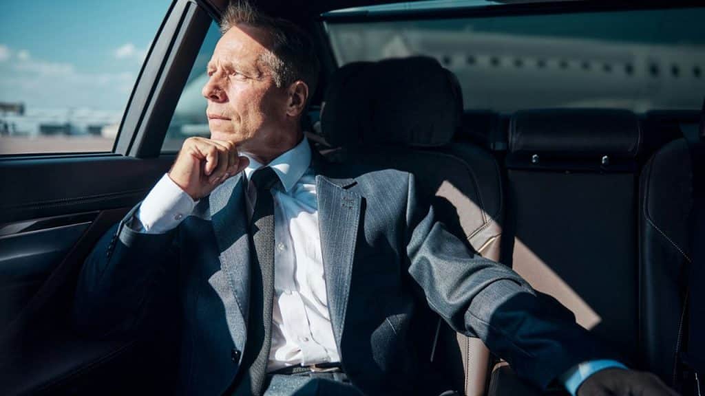 Man in a suit and tie sitting in the back seat of a car, looking out the window.