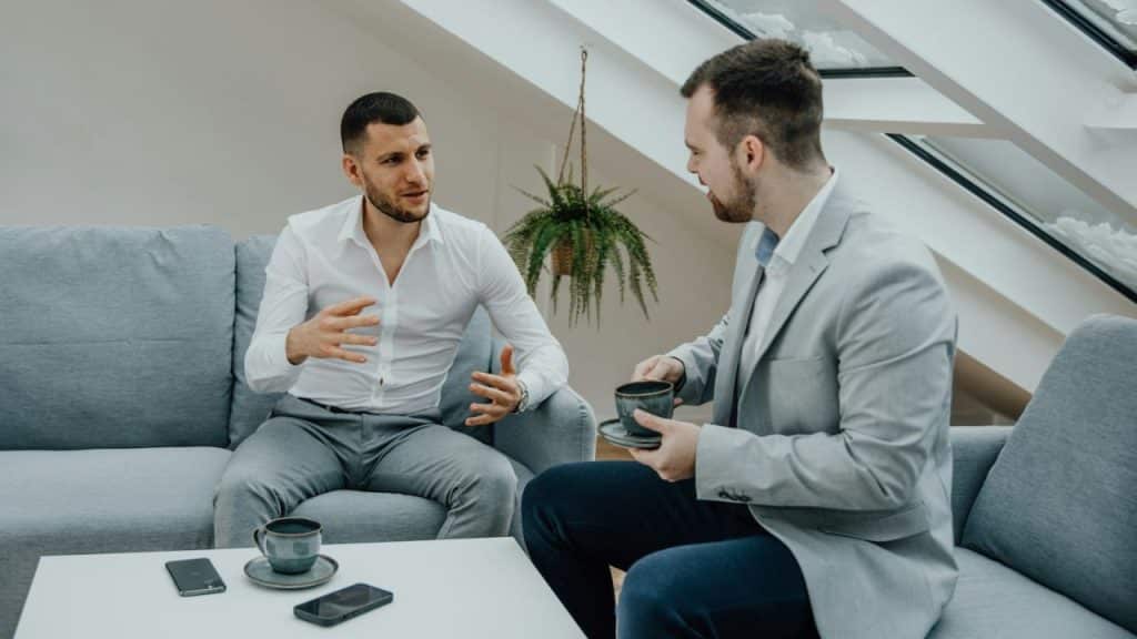 Two men are having a serious conversation while seated on a light blue couch indoors.