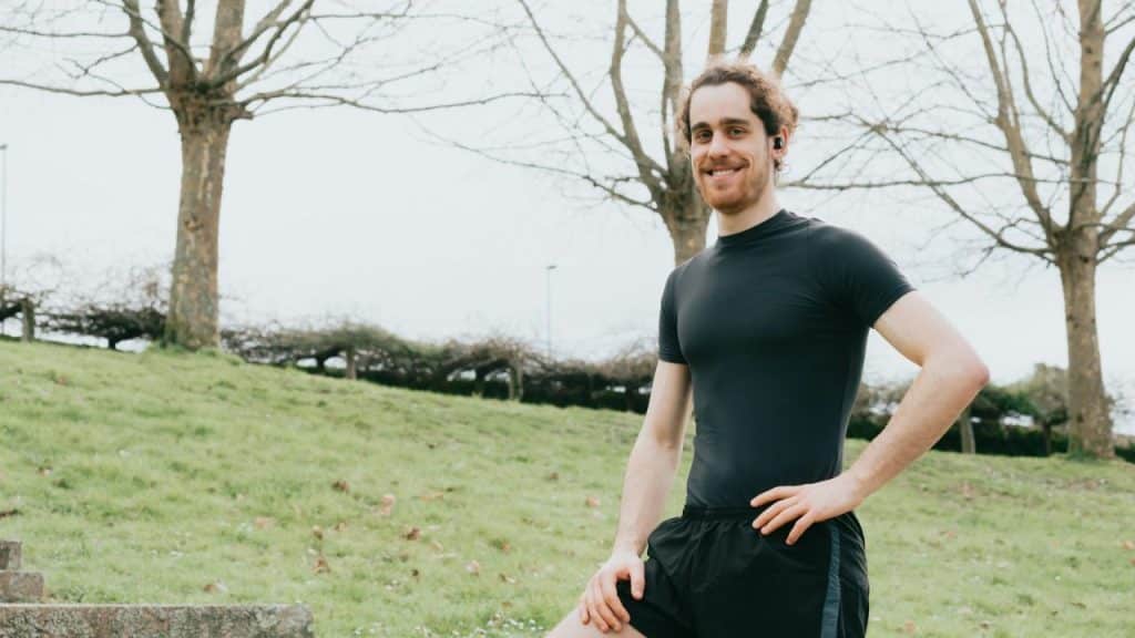 Smiling, fit man in a black T-shirt and shorts standing outdoors in a park.