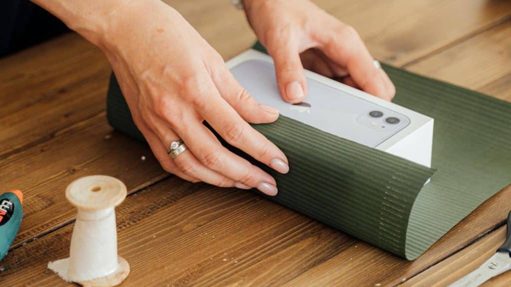 A person wrapping a smartphone box with green paper.