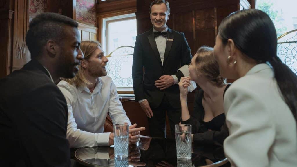 A group of people sitting at a table talking with a waiter standing nearby.