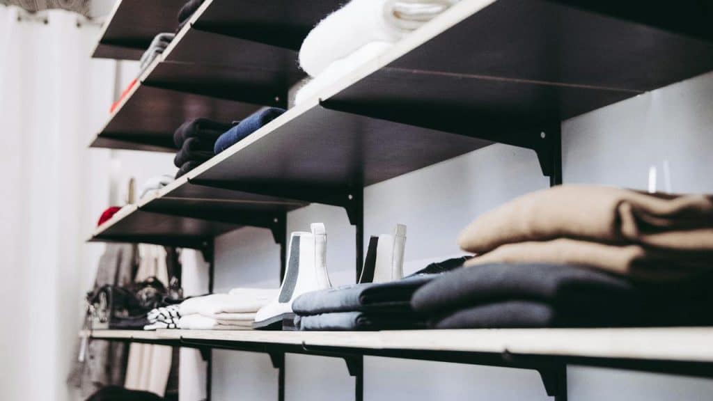 A shelf with neatly folded clothes and a pair of white boots.