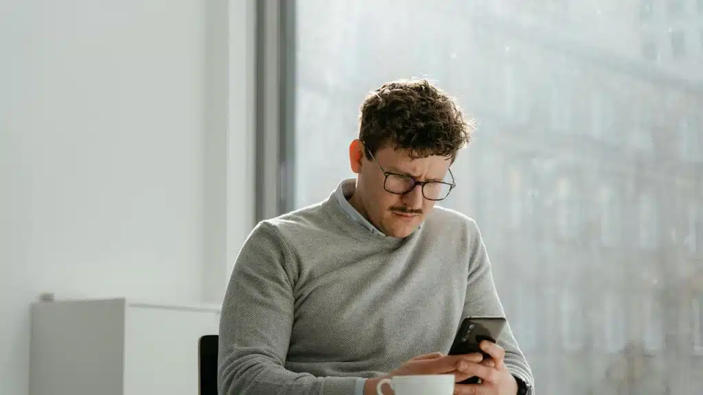 A man sitting by a window looking at his phone.
