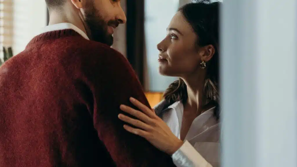 A woman gently touching a man’s shoulder while they look at each other.