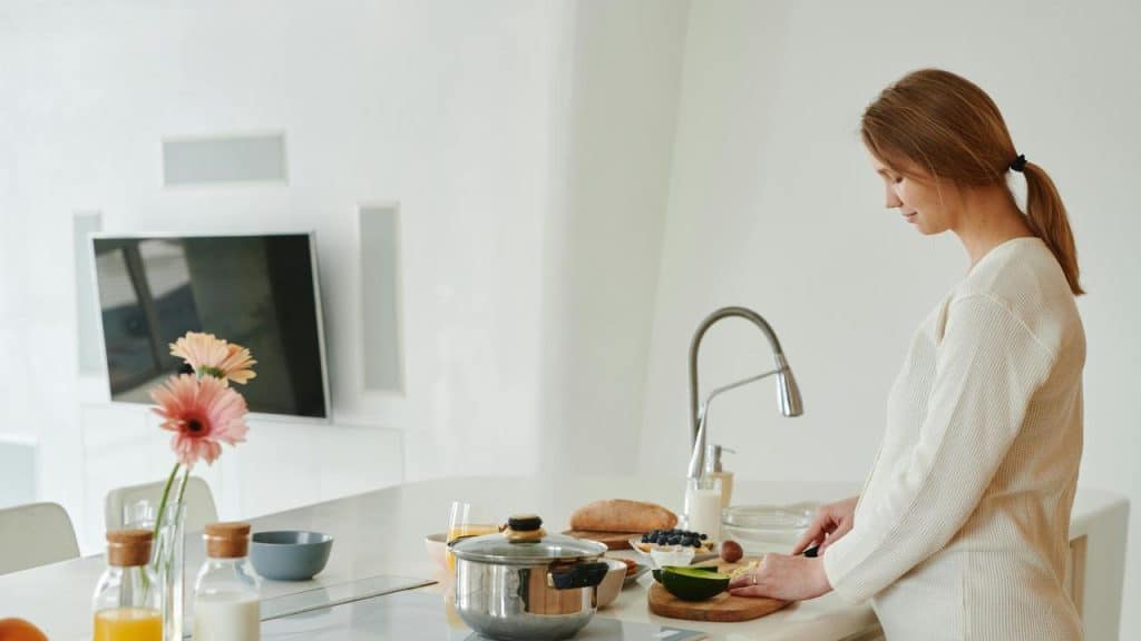 A woman standing in a kitchen slicing avocado on a cutting board.