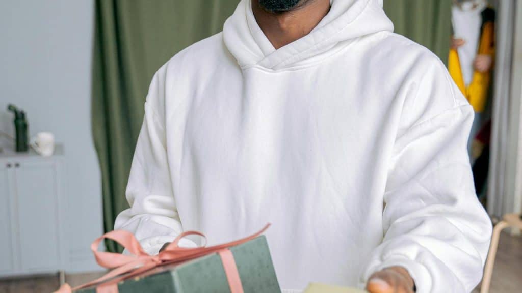 A man in a white hoodie holding a wrapped gift with a pink ribbon.
