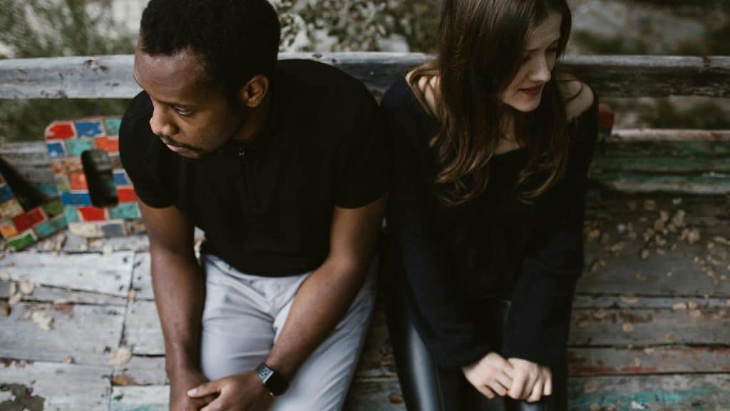 A man and a woman sitting on a bench looking away from each other.
