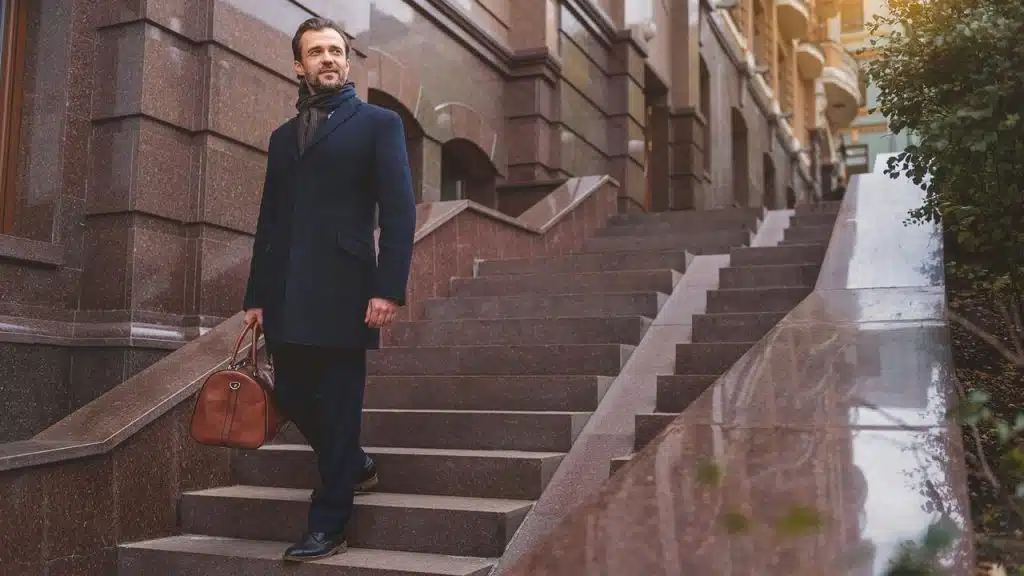 A man walking down outdoor steps holding a leather bag.