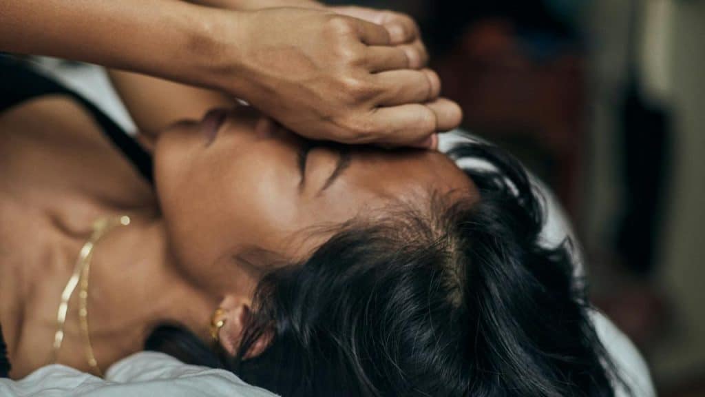 A woman lying on a bed with her hand covering her face.