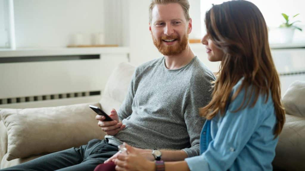 A man and woman sitting on a couch smiling and talking.