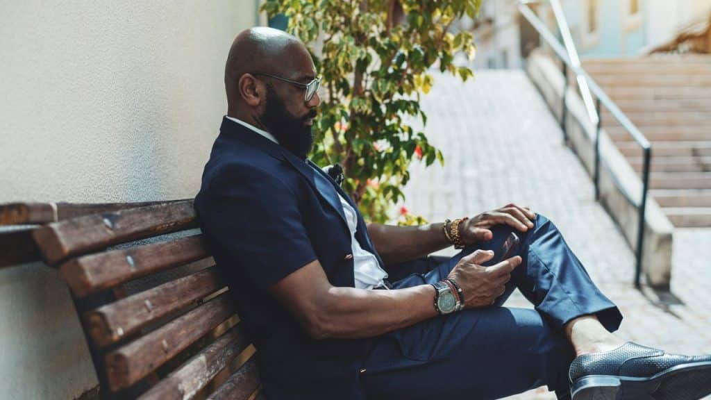 A man sitting on a wooden bench outdoors looking at his phone.