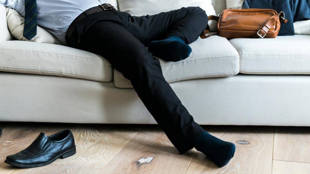 A man in business attire lying on a couch with shoes off.