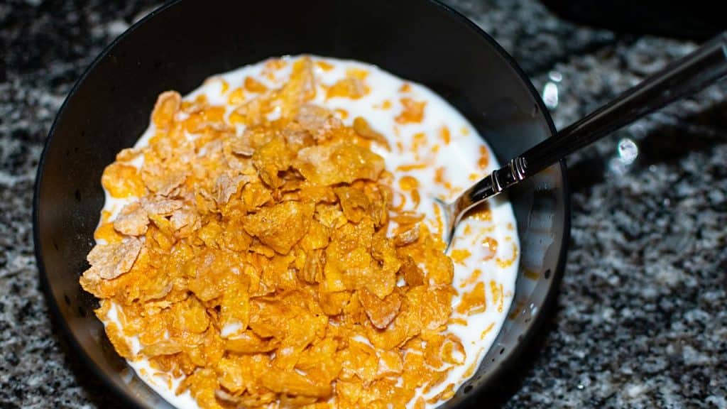 A bowl of cornflakes with milk and a spoon.