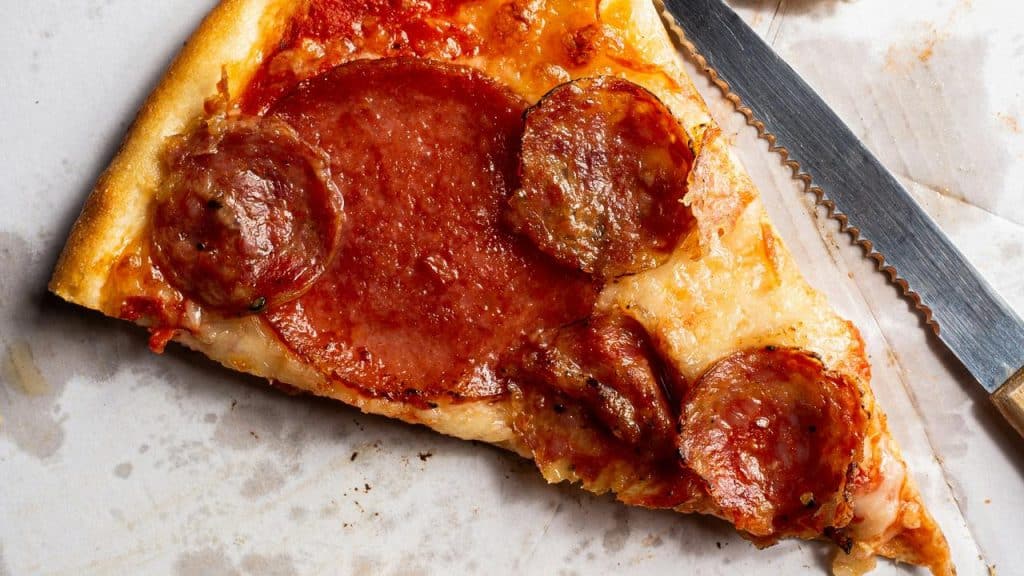 A slice of pepperoni pizza on a plate with a knife.