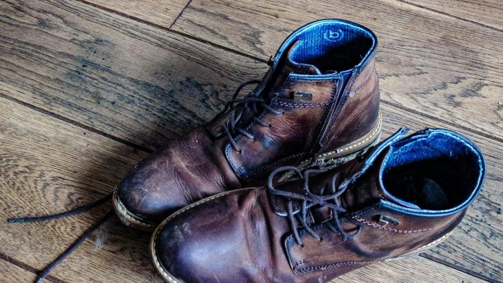 A pair of worn brown leather boots on a wooden floor.