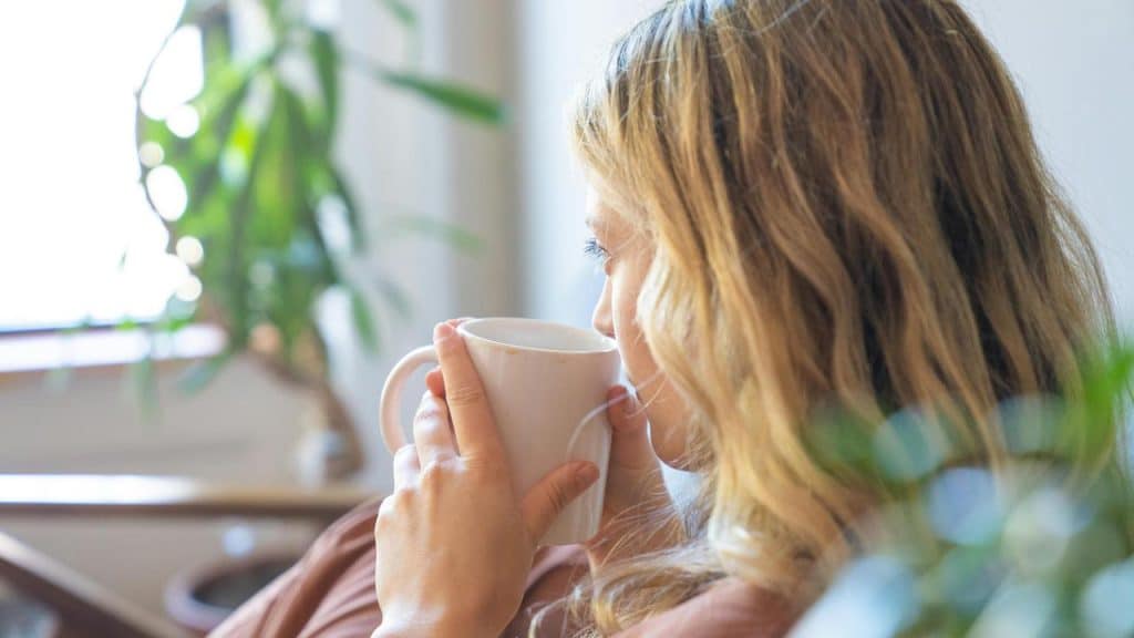 A woman relaxing while drinking from a white mug.