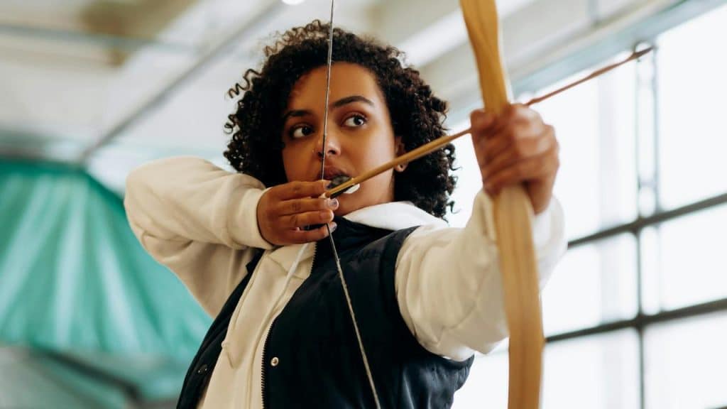 A woman aiming a bow and arrow indoors.