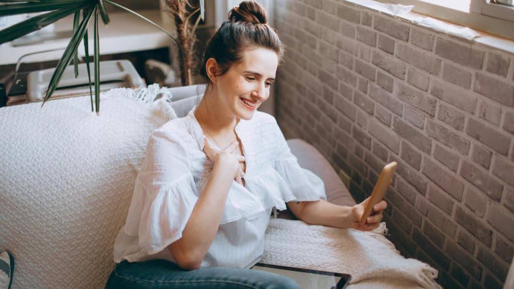 A woman smiling while looking at her phone on a couch.