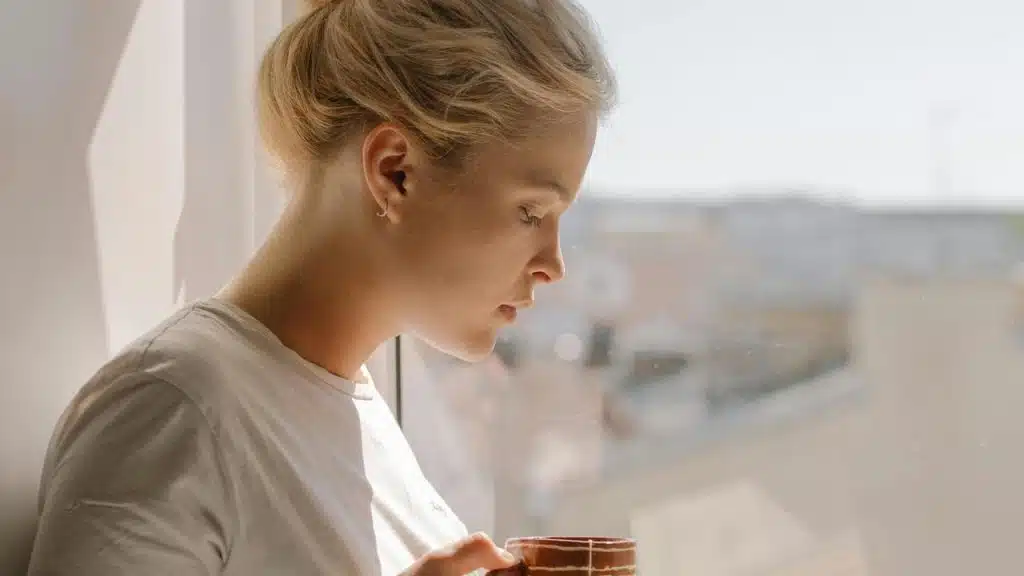 A woman holding a mug while looking out the window.