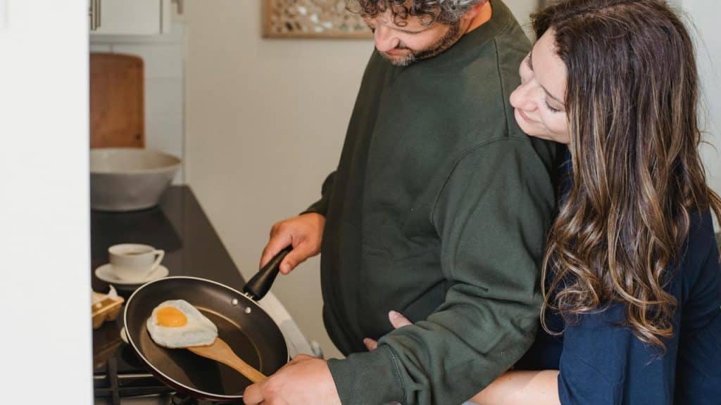 A couple cooking together while making eggs in a frying pan.