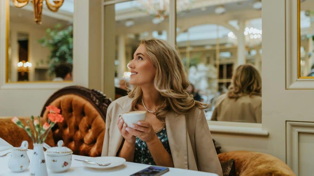 A woman sitting in a cafe holding a cup and smiling.