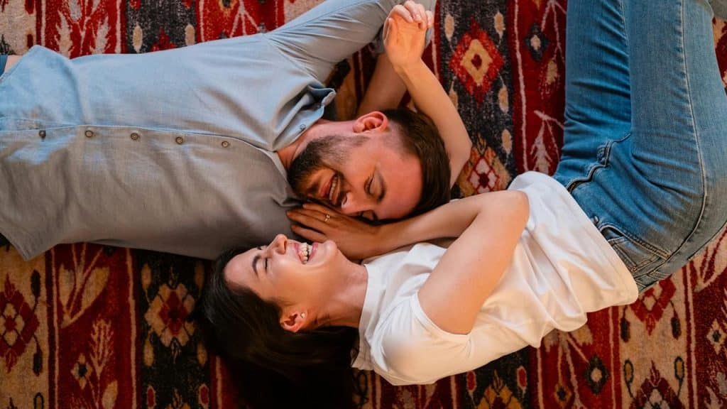 A couple lying on a patterned rug laughing together.