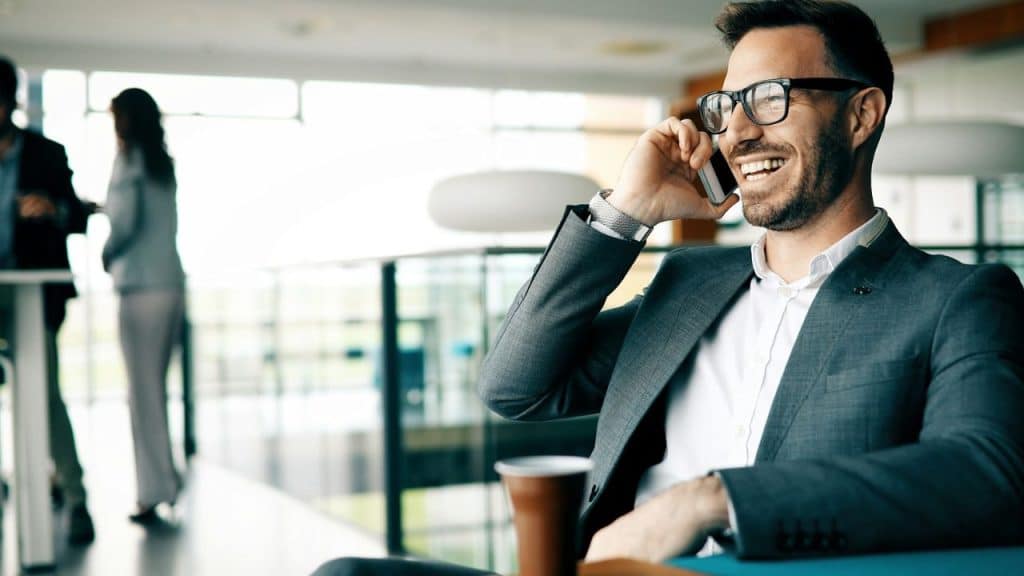 A handsome businessman wearing glasses smiles while talking on a cell phone indoors.