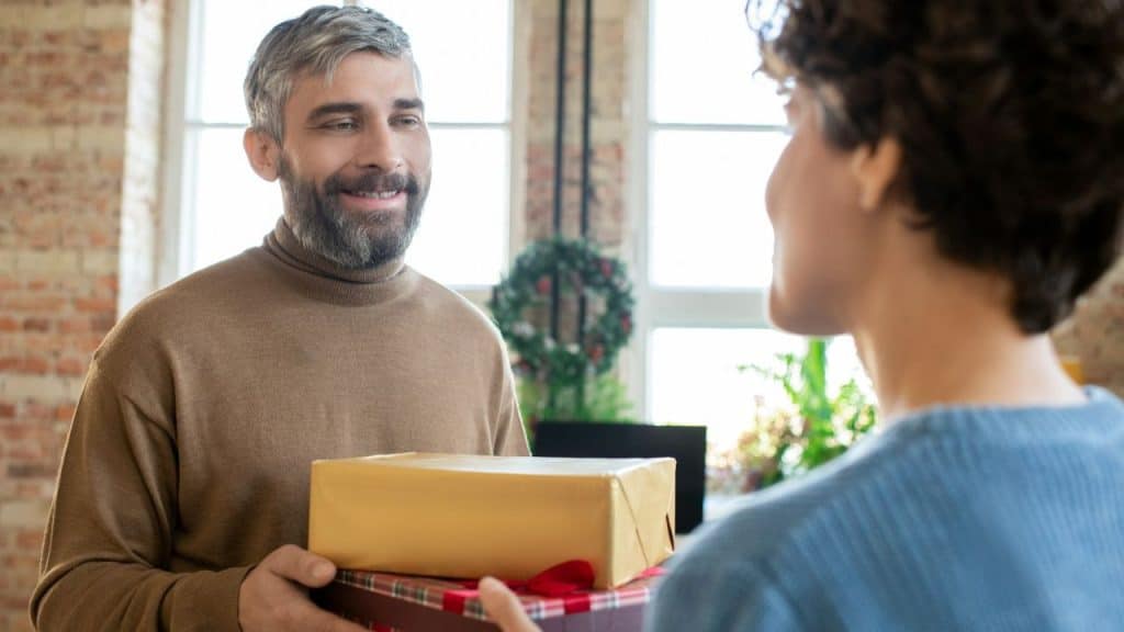 A smiling, bearded man offers a wrapped gift box to a woman.