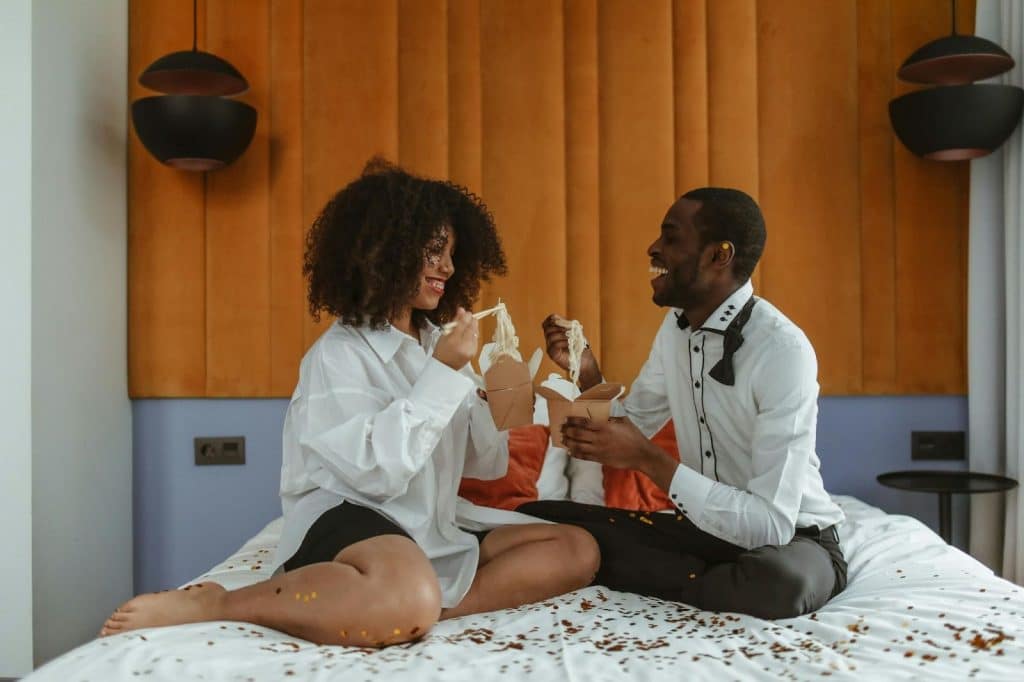 A man and woman happy eating at the bed