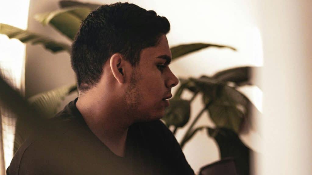 A close-up side profile of a young man next to a large plant.