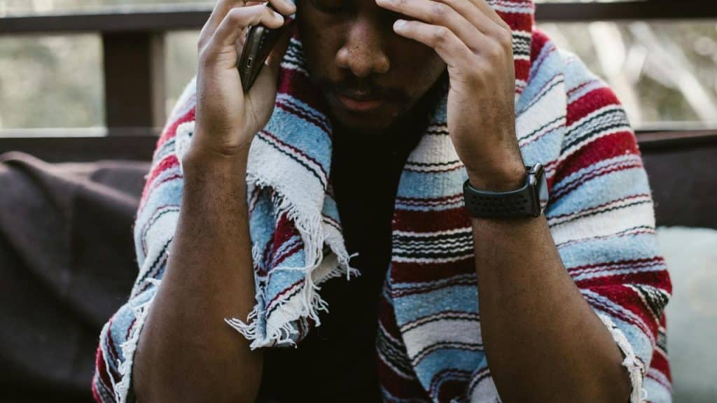 A man wrapped in a striped blanket talking on the phone with a worried expression.