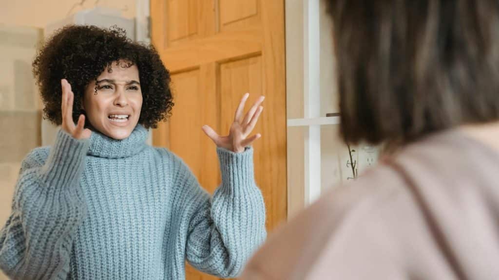 A woman in a blue sweater raising her hands while arguing with someone.